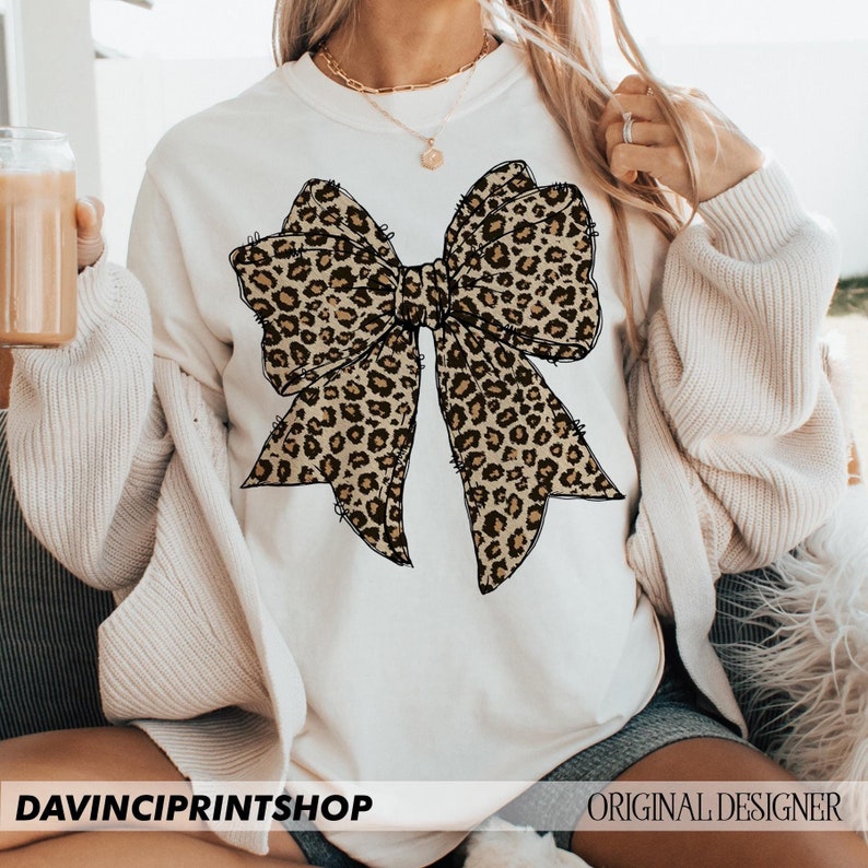 May include: White sweatshirt with a large leopard print bow design.
