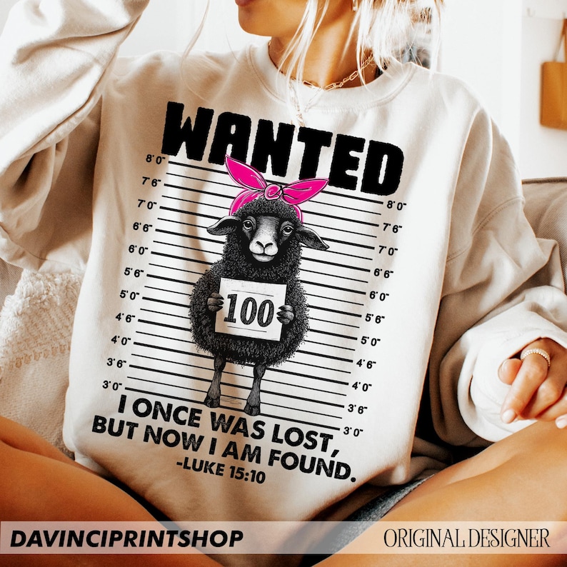 Puede incluir: Una sudadera blanca con un gr&aacute;fico en blanco y negro de una oveja negra con un lazo rosa. El gr&aacute;fico est&aacute; en estilo de cartel de b&uacute;squeda con una tabla de altura y el texto "WANTED" en la parte superior. La oveja sostiene un cartel que dice "100". El texto "I ONCE WAS LOST, BUT NOW I AM FOUND." est&aacute; debajo del gr&aacute;fico, con la referencia b&iacute;blica "LUKE 15:10" debajo.