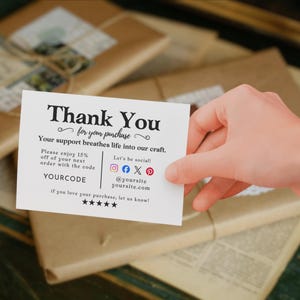 May include: A white card with the words "Thank You" and "for your purchase" in black script. The card includes social media icons and a discount code. The card is held over wrapped packages.