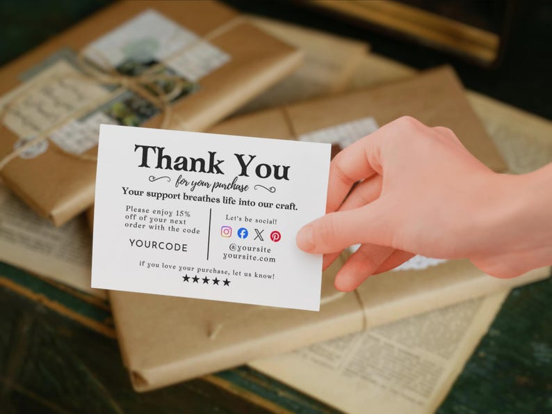 May include: A white card with the words "Thank You" and "for your purchase" in black script. The card includes social media icons and a discount code. The card is held over wrapped packages.