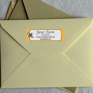 May include: A light yellow envelope with a bee-themed label. The label features a cartoon bee, honeycomb pattern, and the text "Your Farm" along with address and website information. Additional envelopes are visible.