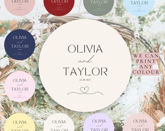 May include: A selection of circular wedding design elements with the names "Olivia and Taylor" and the date "21.09.2027". The design includes a heart symbol and the text "We can print any colour". Various colour options are displayed.