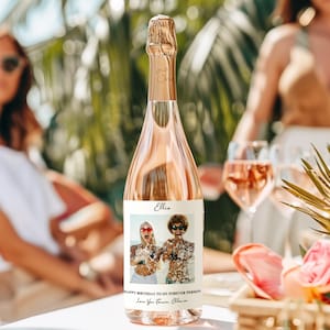 May include: A rose-colored champagne bottle with a gold foil top. The label features a photo of two people and the text "Happy Birthday to my Forever Person." The bottle is on a table with glasses of rose wine.