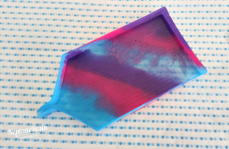 May include: A rectangular silicone mold with a house shape. The mold is filled with a blue, pink, and purple resin mixture. The resin has a cloudy, swirled appearance.