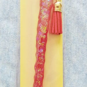 May include: A pink diamond art pen with a gold tassel. The pen is packaged on a yellow card with the text "CUSTOM DIAMOND ART PEN".