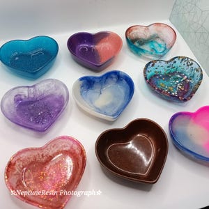 May include: Assortment of heart-shaped resin trinket dishes in various colours, including blue, purple, pink, brown, and white. Each dish has a unique swirl pattern and glitter accents.