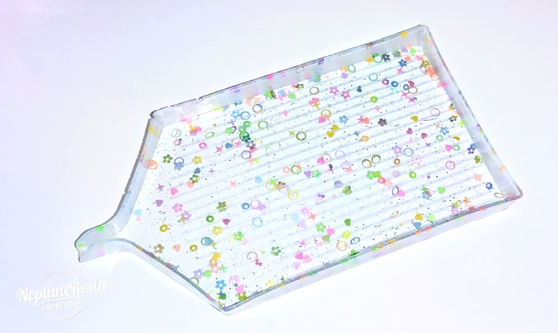 May include: A clear plastic diamond painting tray with a textured surface and a handle. The tray is decorated with colorful glitter and small shapes, including hearts, stars, and circles.