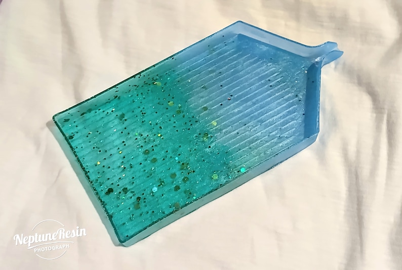 May include: A blue and green resin tray with a textured surface and glitter embedded in the resin. The tray has a handle on the top right corner.