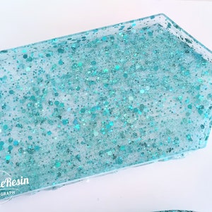 May include: A turquoise resin tray with a handle. The tray is filled with turquoise glitter.