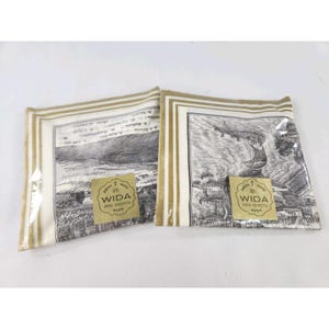 May include: Two paper napkins with black and white landscape illustrations and gold borders. Each napkin has a WIDA label. The napkins are packaged in clear plastic.