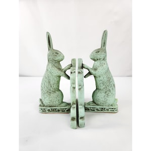 May include: A pair of light green bookends, each featuring a rabbit standing on its hind legs with front paws resting against a vertical support. The rabbits have a textured finish with darker green accents, and the bases feature decorative scrollwork.