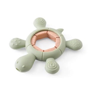 May include: A sage green turtle-shaped baby teether with a natural wood center. The teether has a textured surface on the head and flippers. The center is made of light brown wood.