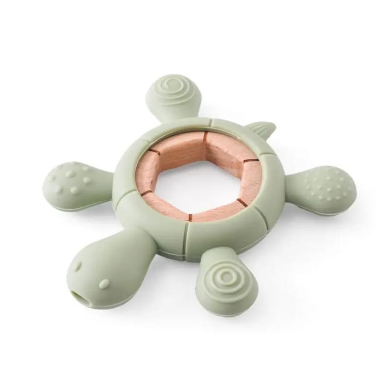 May include: A sage green turtle-shaped baby teether with a natural wood center. The teether has a textured surface on the head and flippers. The center is made of light brown wood.