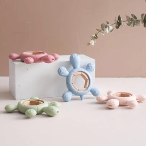 May include: Four colorful turtle-shaped baby teethers. The teethers are in shades of pink, blue, and green, with a wooden ring in the center. The teethers are designed with textured surfaces for soothing gums.