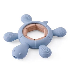 May include: A blue silicone baby teether shaped like a turtle. The teether has a wooden center and textured details on the flippers and head. The teether is designed for babies to chew on to soothe sore gums.