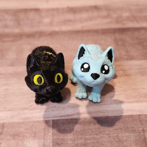 May include: Two small animal figurines, one black and one light blue, with large eyes and a cartoonish style.