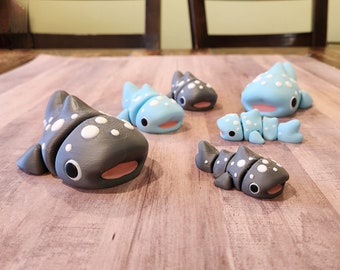 May include: A collection of handmade clay whale shark figurines in various poses. The figurines are primarily gray and light blue, with white spots and pink accents. The collection includes several complete whale sharks and one segmented version.