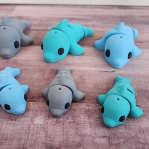 May include: Six small dolphin figurines in various shades of blue and grey. The dolphins are made of a smooth, plastic-like material and have black eyes.