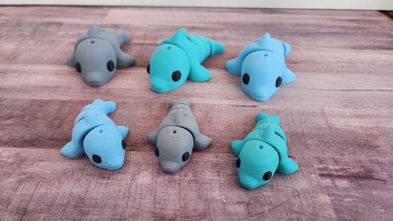 May include: Six small dolphin figurines in various shades of blue and grey. The dolphins are made of a smooth, plastic-like material and have black eyes.