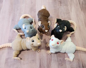 Puede incluir: Seis figuras de ratas en varios colores: marrón, negro, blanco y tonos de gris. Cada rata tiene una cola larga y pálida y pequeñas patas detalladas. Las figuras están dispuestas sobre una superficie de madera clara.