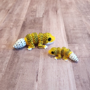 May include: Two yellow and black gecko figurines with white spots. The larger gecko has a white tail and the smaller gecko has a white tail tip.