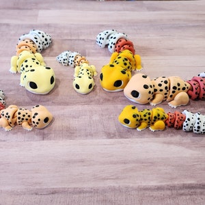 May include: Five colorful segmented gecko figurines made of polymer clay. The geckos are in various poses and have black spots on their bodies. The geckos are yellow, orange, red, and white.