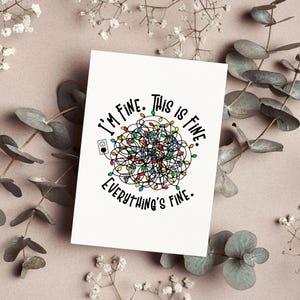 Puede incluir: Una tarjeta de felicitación blanca con el texto "I'm fine. This is fine. Everything's fine." La tarjeta presenta una maraña de luces navideñas de colores y una ilustración de enchufe. La tarjeta está rodeada de vegetación decorativa.