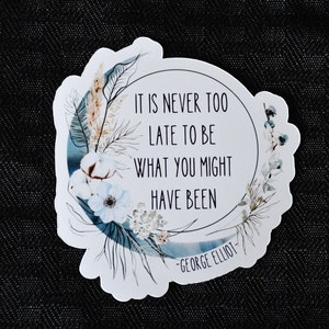 May include: A white sticker with a blue crescent moon and floral design. The text reads "It is never too late to be what you might have been - George Eliot -"