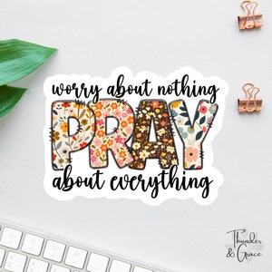 Op de afbeelding: Een witte sticker met de tekst "worry about nothing PRAY about everything" in het zwart. Het woord "PRAY" staat in grote letters en is versierd met een bloemenpatroon.