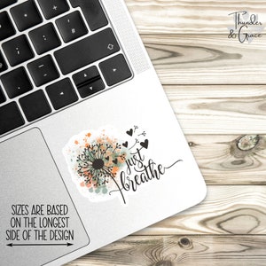 May include: A white laptop with a sticker that says "just breathe" with a dandelion design and watercolor accents. The sticker is on the top right corner of the laptop.