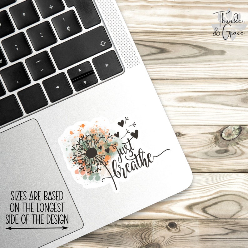 May include: A white laptop with a sticker that says "just breathe" with a dandelion design and watercolor accents. The sticker is on the top right corner of the laptop.