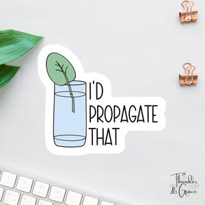 May include: A white sticker with a cartoon illustration of a leaf in a glass of water. The sticker has the text "I'd Propagate That" in black. The sticker is on a white surface with two gold paper clips.