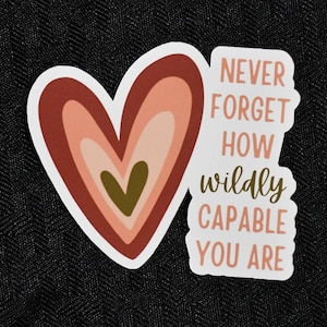 May include: A sticker with a heart design in shades of red, pink, and green. The text on the sticker reads "Never forget how wildly capable you are."