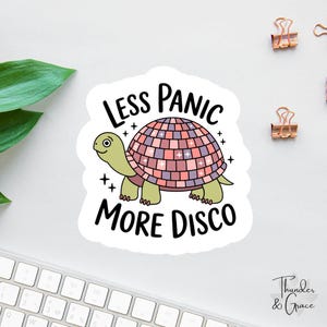 May include: A die-cut sticker featuring a light green turtle with a pink and purple disco ball shell. The text "LESS PANIC MORE DISCO" is printed in black above and below the turtle, accented by small black star symbols surrounding the design.