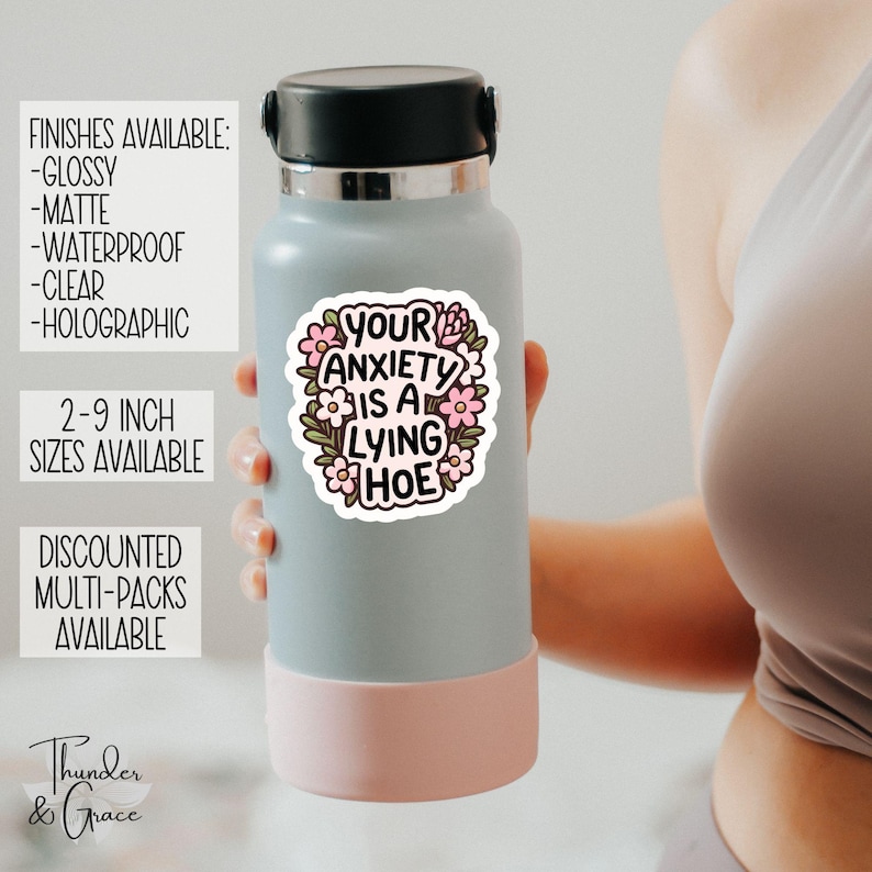 May include: A light blue water bottle with a black lid and a pink base. A sticker on the bottle reads "YOUR ANXIETY IS A LYING HOE" surrounded by pink flowers and green leaves. The sticker is available in sizes 2-9 inches.