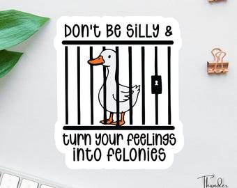 May include: A white sticker with the text "Don't Be Silly & turn your feelings into felonies." The sticker features a cartoon duck inside a cage. The duck has an orange beak and feet. The sticker has a white background.