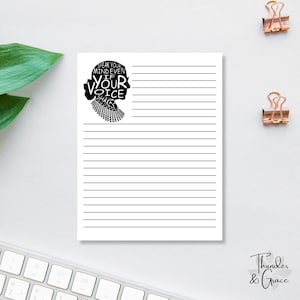 Op de afbeelding: Een wit gelijnd notitieblok met een zwart silhouet van een vrouwenprofiel en de quote: "Speak Your Mind Even If Your Voice Shakes". Gouden paperclips en een toetsenbord zijn ook zichtbaar.