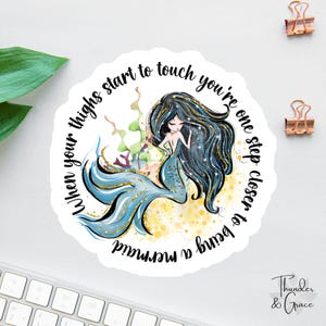 May include: A round sticker featuring a mermaid illustration with long black and blue hair and a blue tail. The text "When your thighs start to touch you're one step closer to being a mermaid" is written around the mermaid.