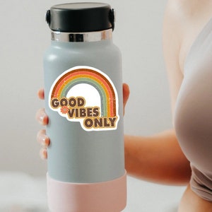 May include: A gray water bottle with a pink bottom and a rainbow sticker that says "Good Vibes Only".