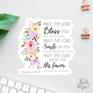May include: A white sticker with floral accents and the text "May the Lord Bless You." The sticker features a watercolor design with pink, peach, and purple flowers. The text is in a handwritten style.