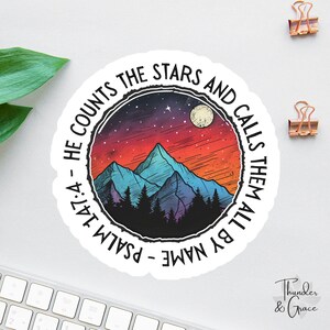 May include: A round sticker featuring a mountain landscape with a night sky. The design includes a full moon, stars, and pine trees. The text around the edge reads "He counts the stars and calls them all by name - Psalm 147:4."