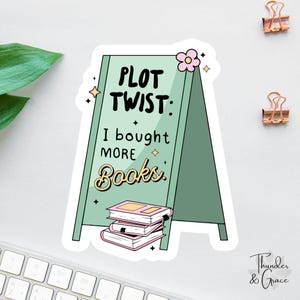 May include: A sticker with a green sign that reads "PLOT TWIST: I bought MORE Books." The sign has a pink flower and a stack of books at the bottom. The sticker is on a white surface.