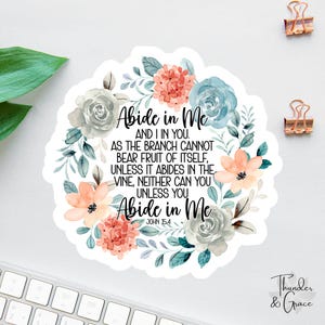 Puede incluir: Una pegatina blanca con el texto "Abide in Me" rodeada por una corona floral en tonos rosas, azules y grises. La pegatina también incluye el texto "John 15:4" y las palabras "Thunder & Grace".