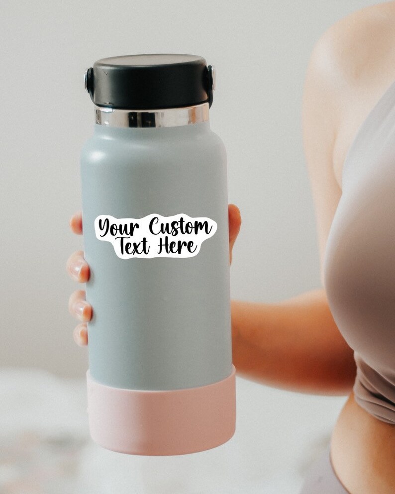 May include: A gray reusable water bottle with a pink silicone base. A white sticker with the text "Your Custom Text Here" is on the bottle.