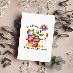 Puede incluir: Una tarjeta de felicitación con una ilustración en acuarela de un gato patchwork en una maceta, con una flor y el texto "I am fearfully & wonderfully made" y Salmo 139:14.