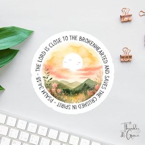 May include: A circular sticker with a watercolour design depicting a sunset over mountains, with the text "THE LORD IS CLOSE TO THE BROKENHEARTED AND SAVES THE CRUSHED IN SPIRIT - PSALM 34:18". The sticker has a white border.