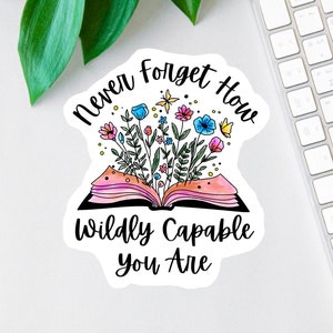 May include: A sticker with an open book with flowers growing out of it. The text reads "Never forget how wildly capable you are."