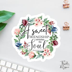 May include: A sticker with a floral wreath design. The text reads "A sweet friendship refreshes the soul" with the Bible verse Proverbs 27:9. The wreath features pink, burgundy, and blue flowers with green leaves. The sticker has a white background.