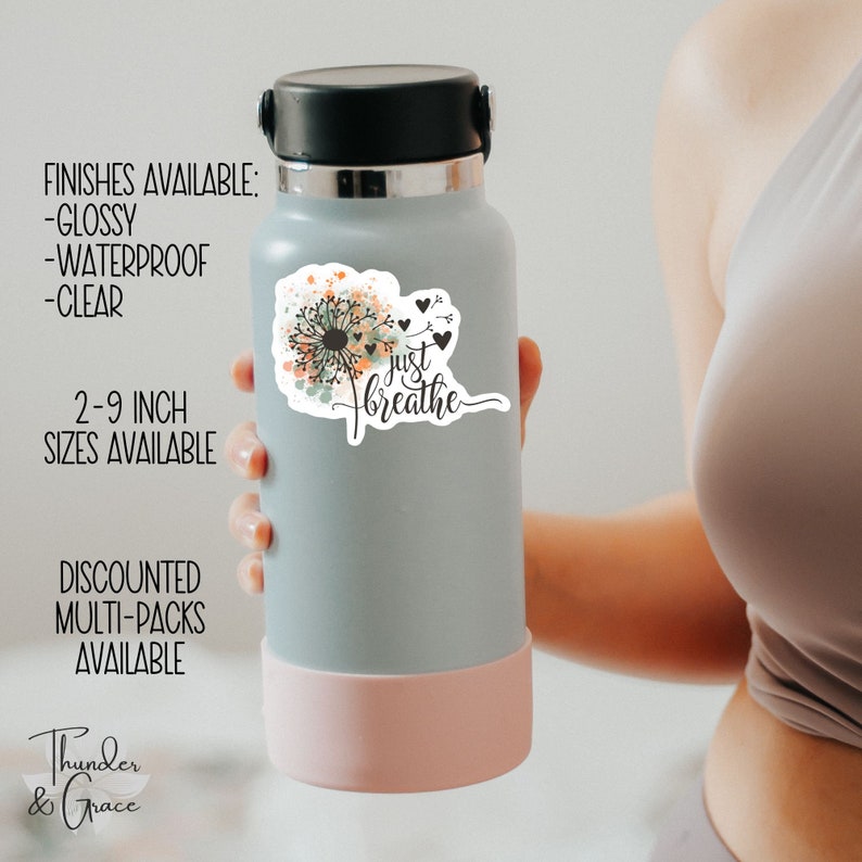 May include: A gray water bottle with a pink lid and a white sticker featuring a watercolor dandelion with the text "just breathe".