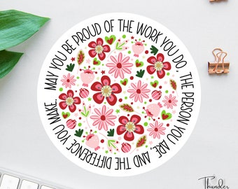 May include: A white round sticker with a floral design in shades of pink and red. The text "May you be proud of the work you do. The person you are, and the difference you make." is written in black around the edge of the sticker.
